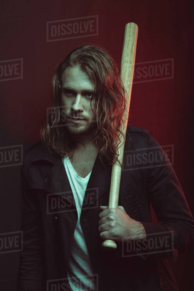 Portrait of serious long haired man holding baseball bat on shoulder