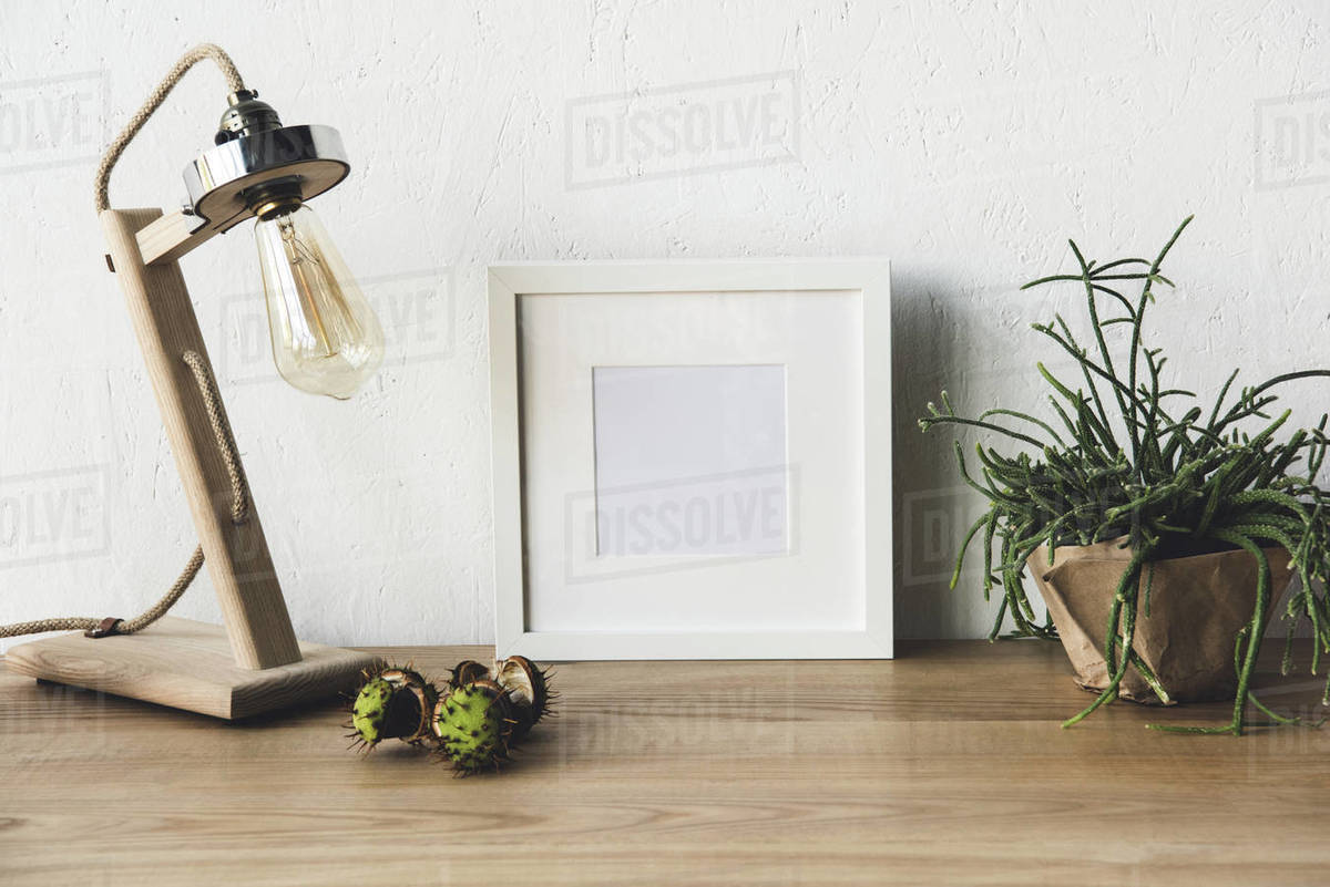 Close up view of empty photo frame, table lamp and plant in flowerpot