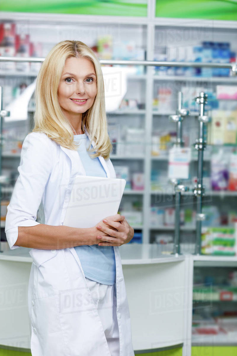 Pharmacist holding digital tablet and smiling at camera in drugstore
