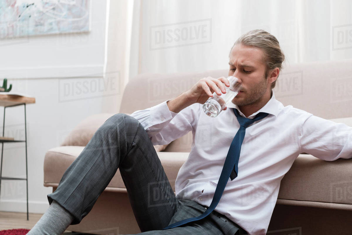 businessman-sitting-on-a-floor-at-home-and-drinking-water-stock-photo