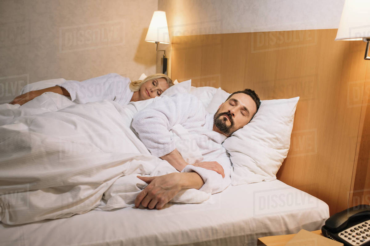 Beautiful middle aged couple in bathrobes sleeping together in bed in