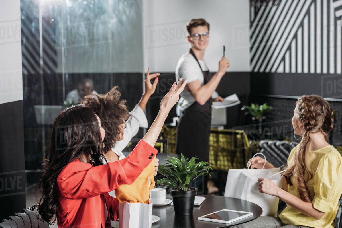Group of stylish multiethnic women calling waiter in cafe Stock Photo