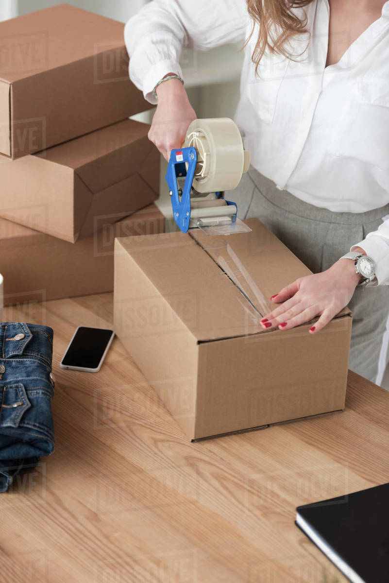 Partial view of entrepreneur packing customers parcel with adhesive
