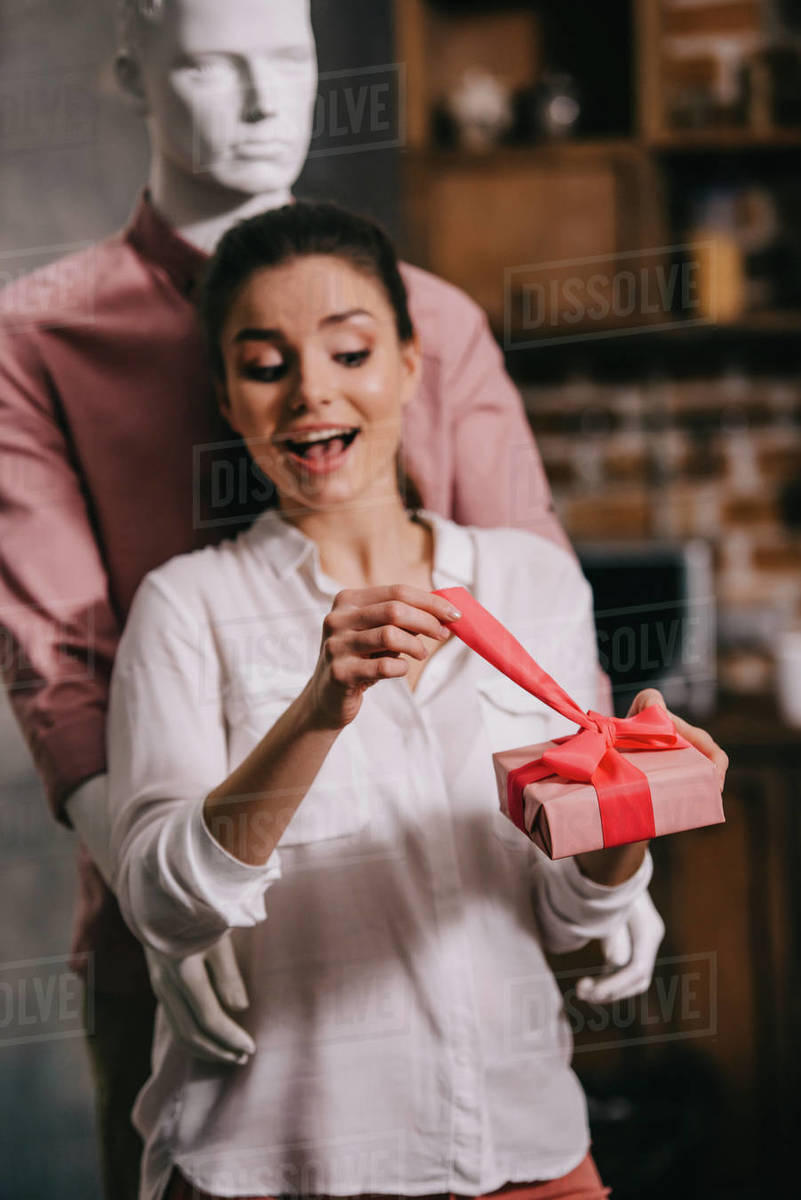 Excited woman opening gift in hands with mannequin hugging her behind, perfect man dream concept