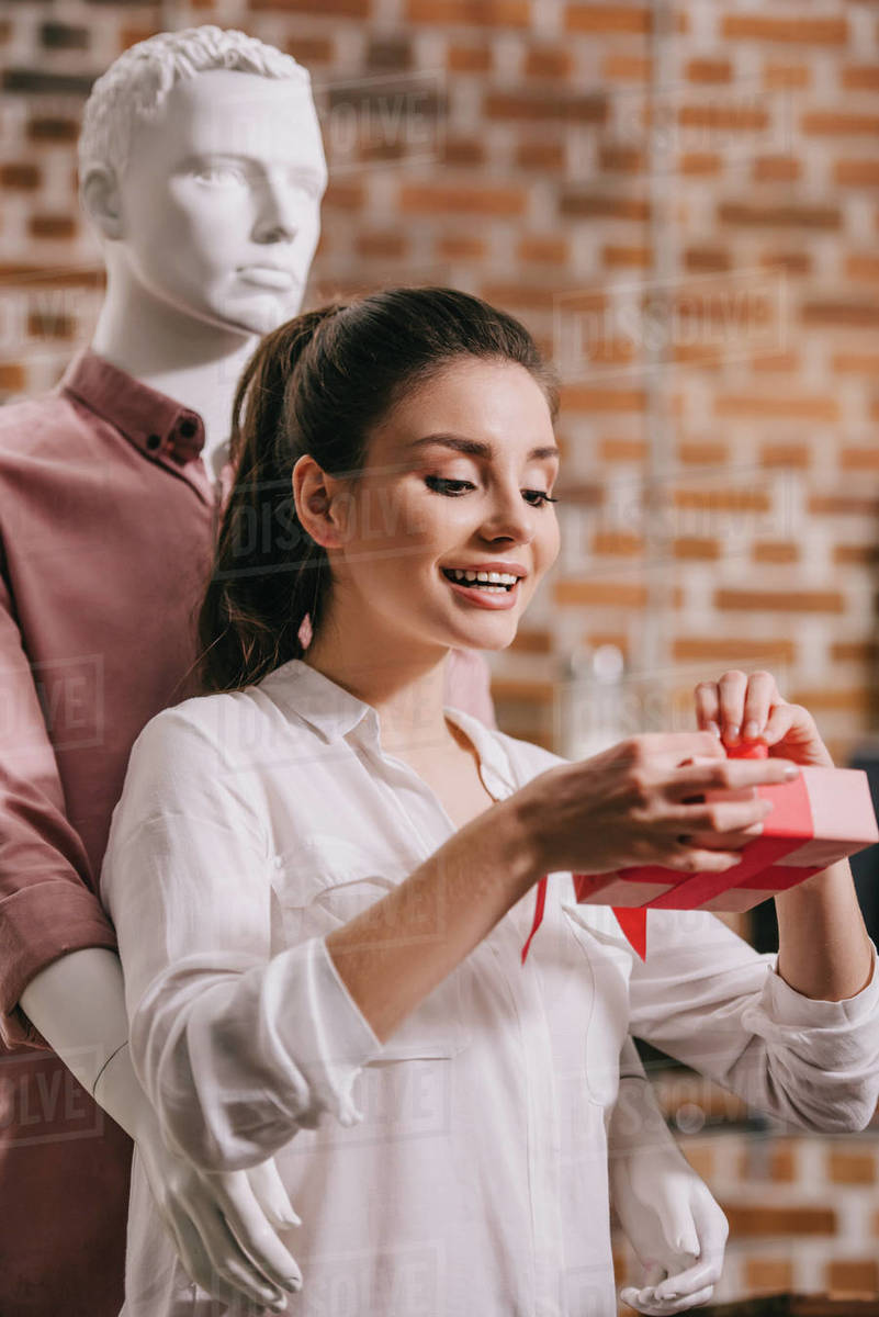 Young woman opening gift in hands with mannequin hugging her behind, perfect man dream concept