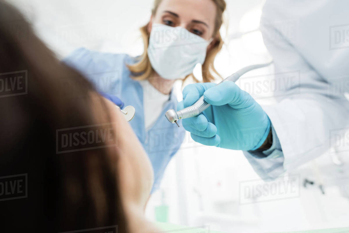 Doctors using dental drill during procedure in modern dental clinic