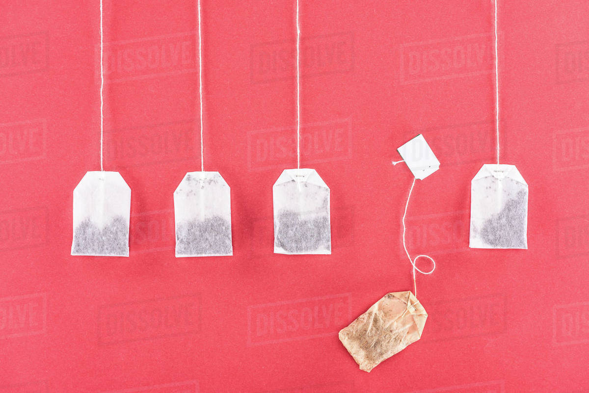 Top view of four unused tea bags and one used tea bag isolated on red