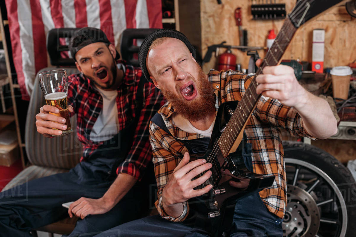 Drunk mechanics playing guitar and drinking beer at garage Stock Photo Dissolve