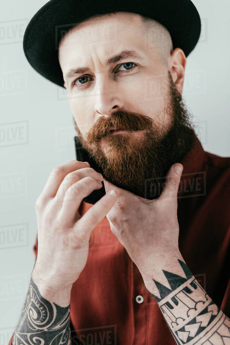 Bearded Handsome Man Combing Beard And Looking At Camera Isolated