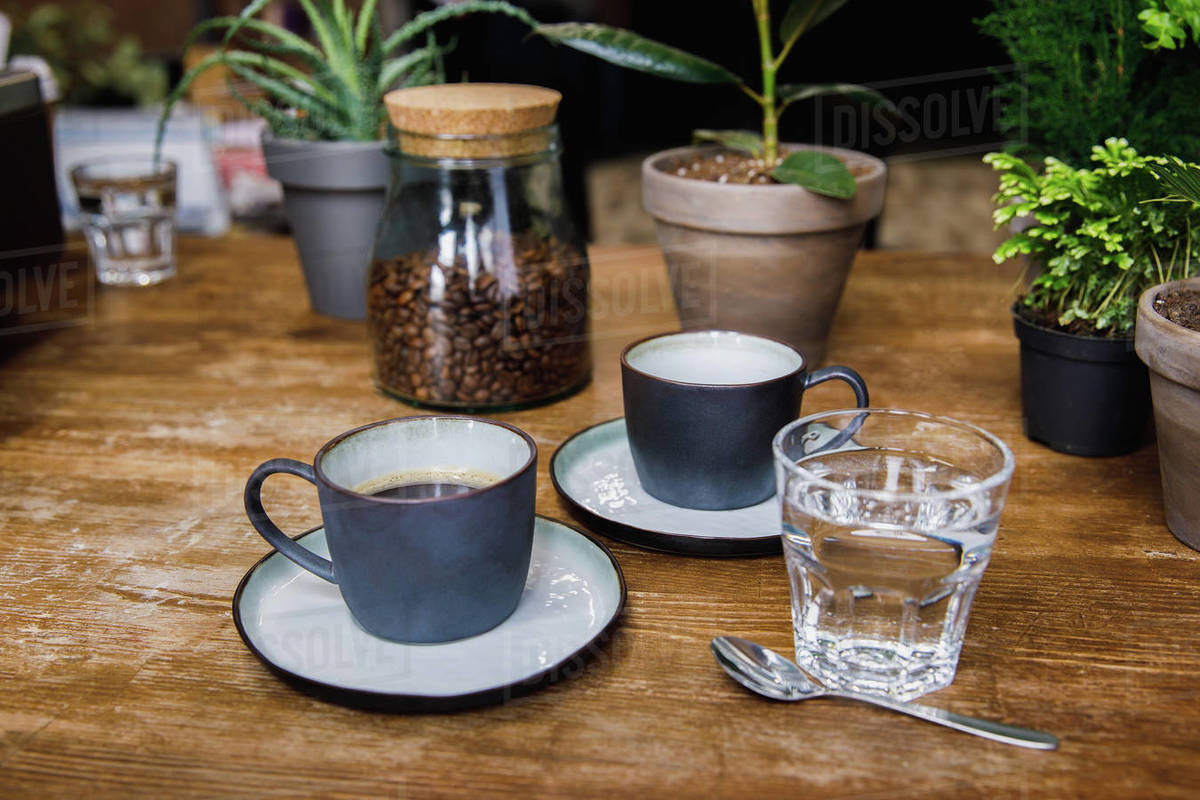 Cups Of Coffee And Glass Of Water On Table In Cozy Coffee Shop Stock Photo Dissolve