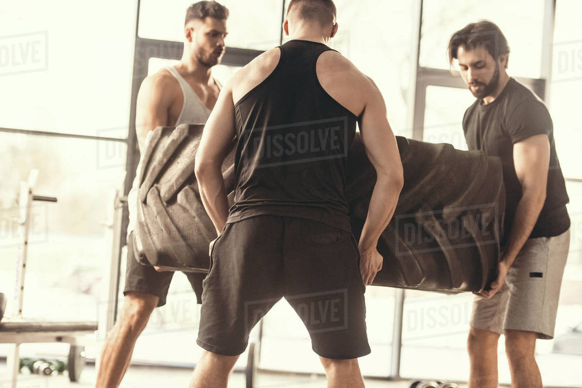 Muscular young sportsmen lifting tire together in gym Stock Photo Dissolve