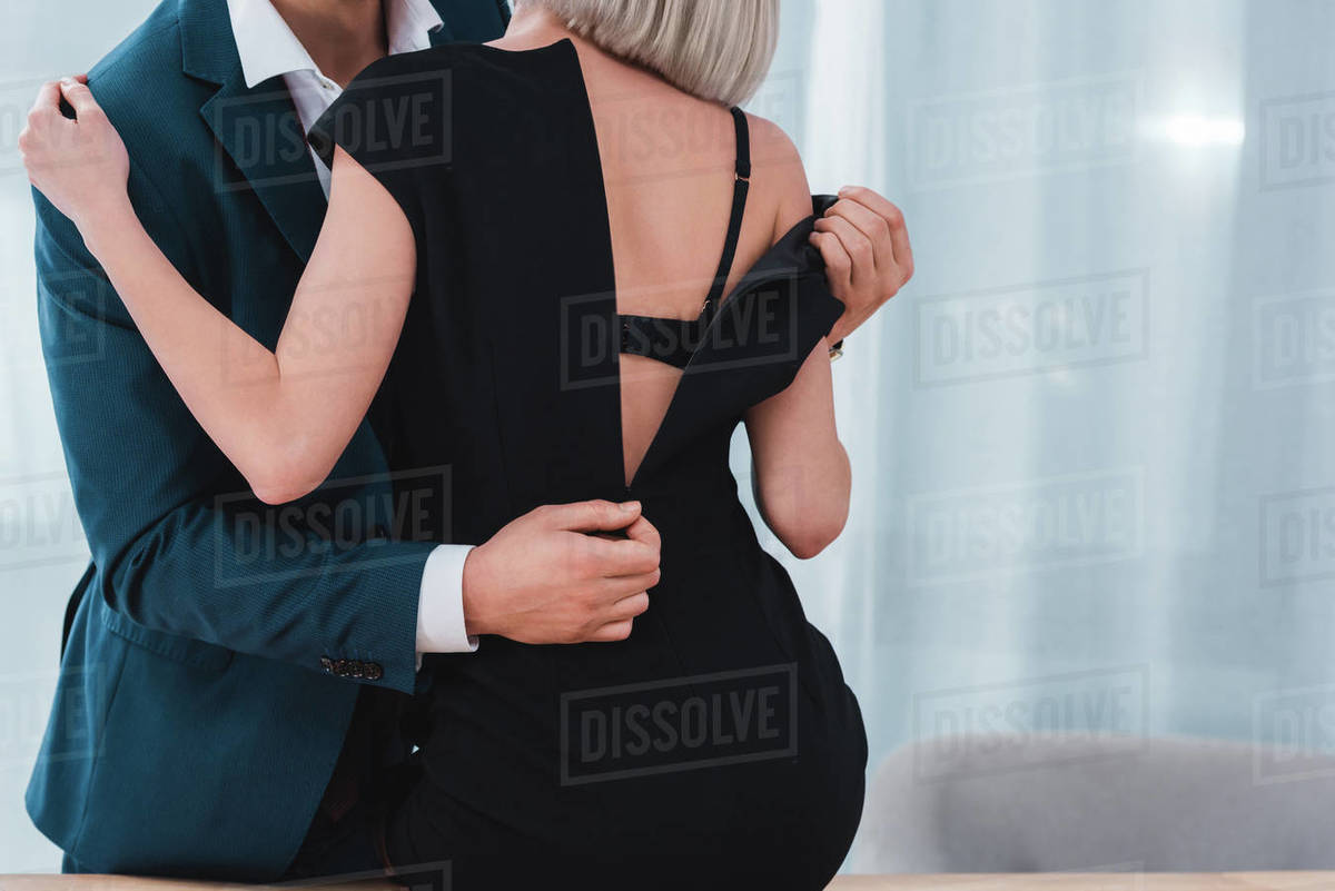 cropped shot of businessman taking off black dress from young female colleague in office Stock