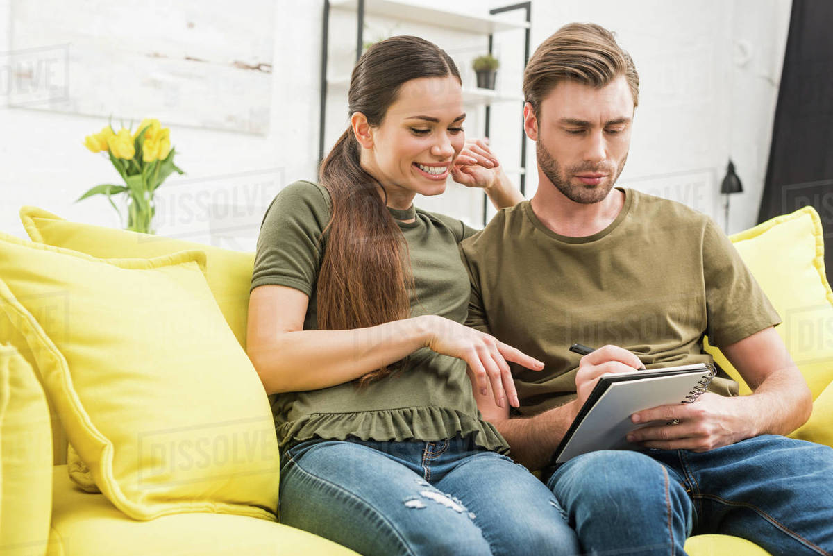 Couple writing in notebook together on cozy couch at home Stock Photo Dissolve