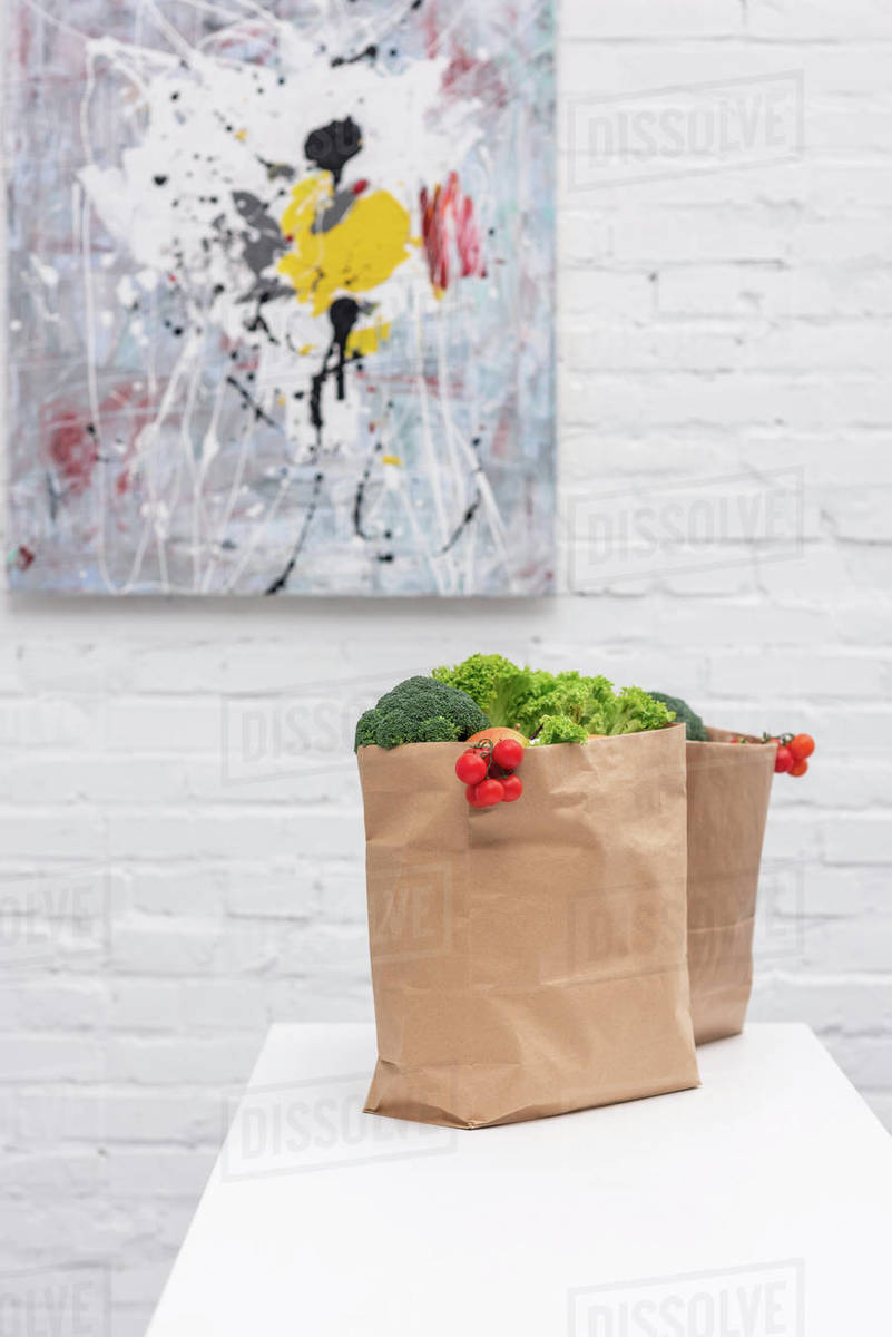 Grocery store bags with vegetables on table in front of white brick