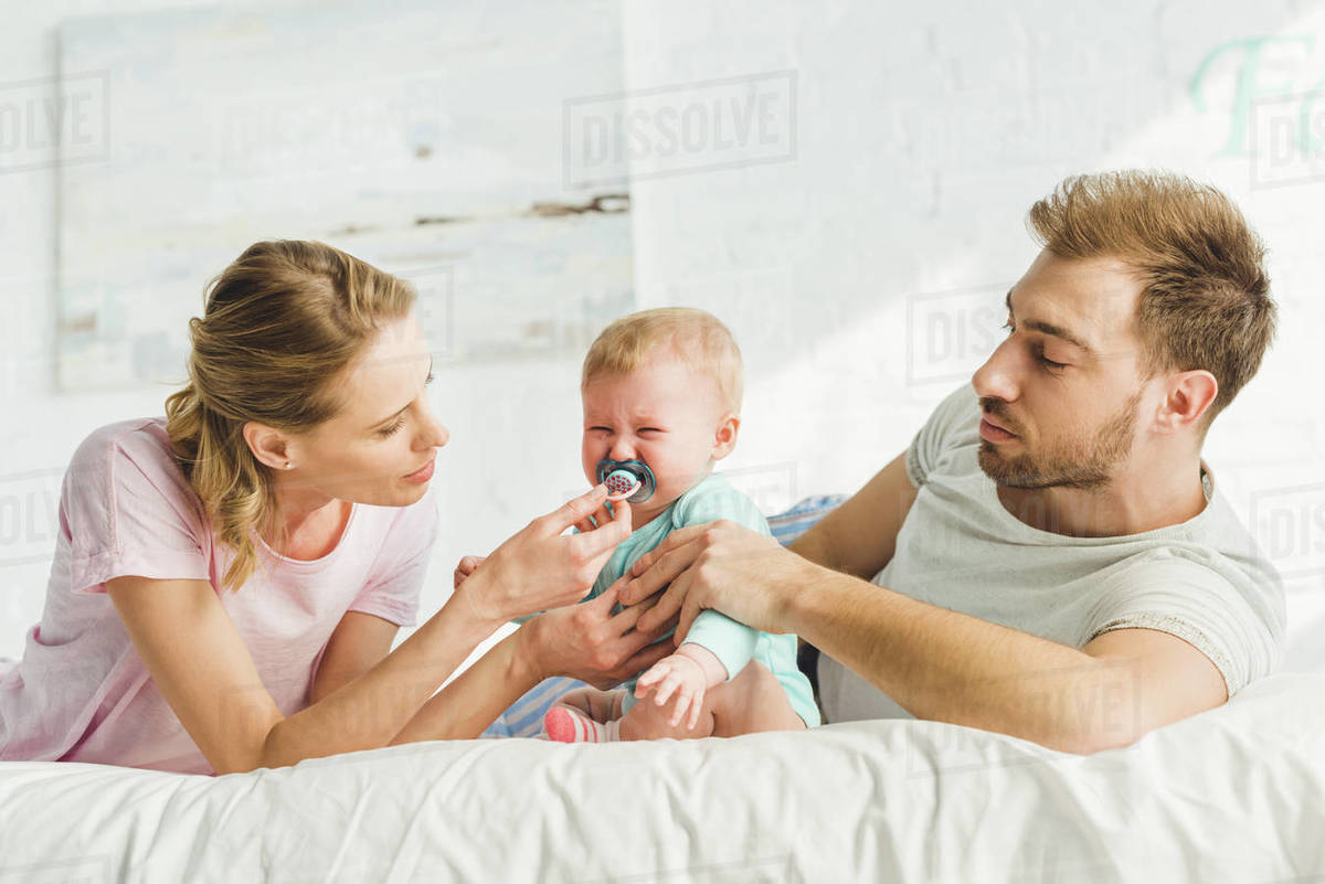 Young parents trying to calm down crying infant daughter with baby