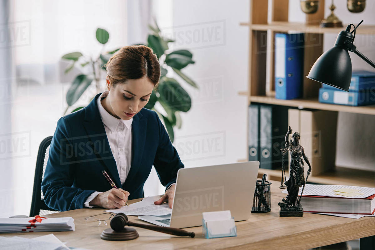 Female lawyer in suit at workplace with laptop, gavel and Femida in