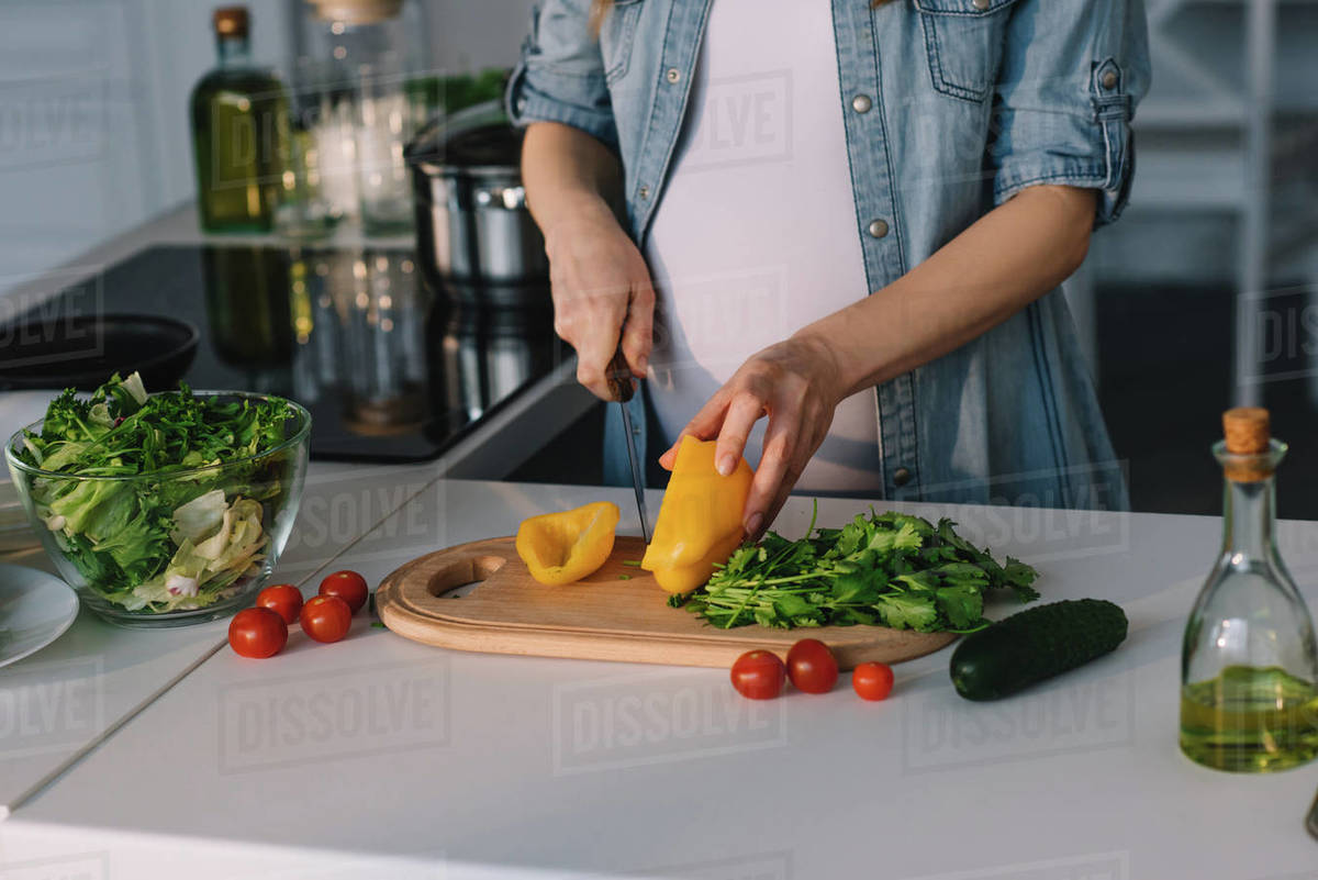 Cropped image of attractive pregnant woman cutting bell pepper for