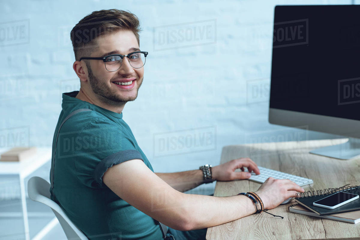 Handsome young man in eyeglasses working with desktop computer and