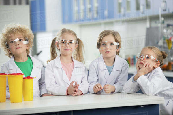 Four kids in science laboratory wearing coats and standing at table ...