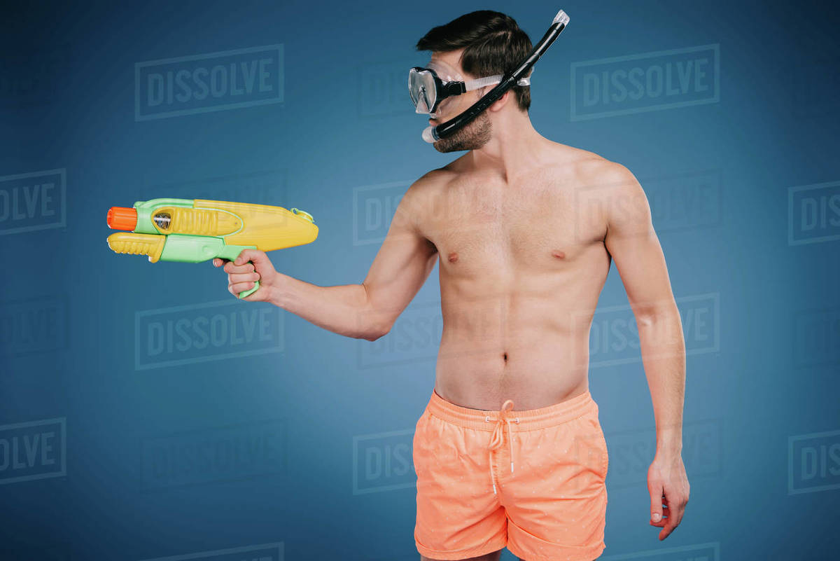 Young man in shorts and diving mask holding water gun on blue Stock