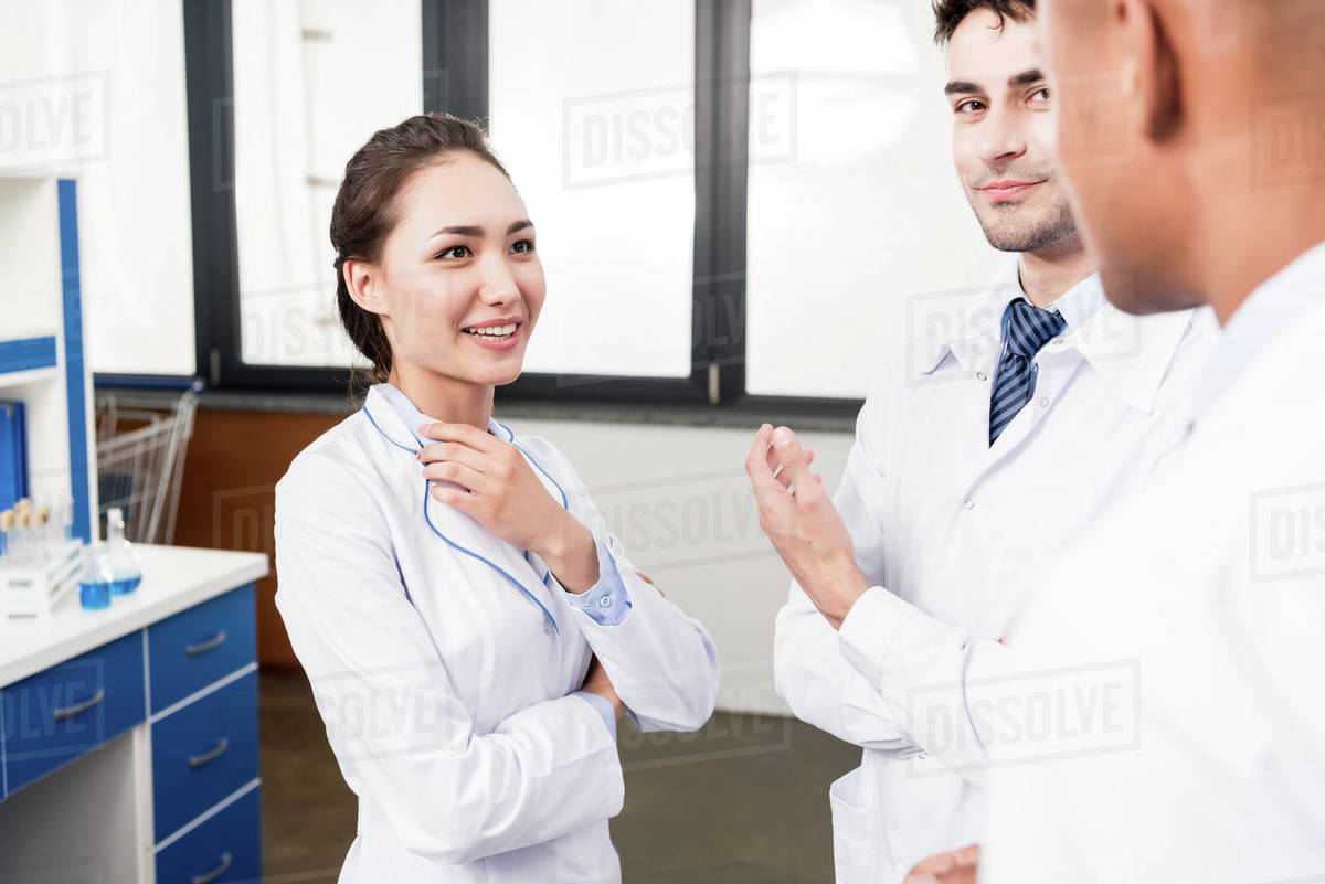 Team of young doctors in lab coats discussing work in laboratory Stock Photo Dissolve