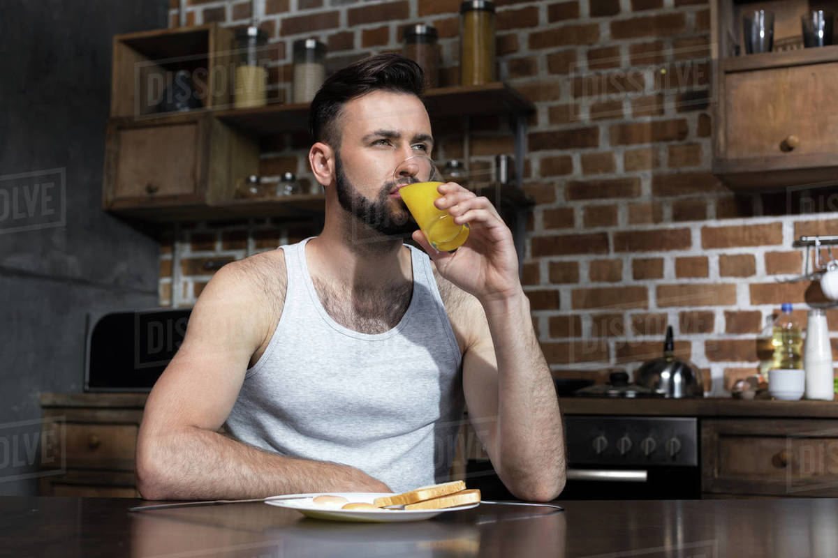 Handsome bearded young man drinking juice while eating breakfast at