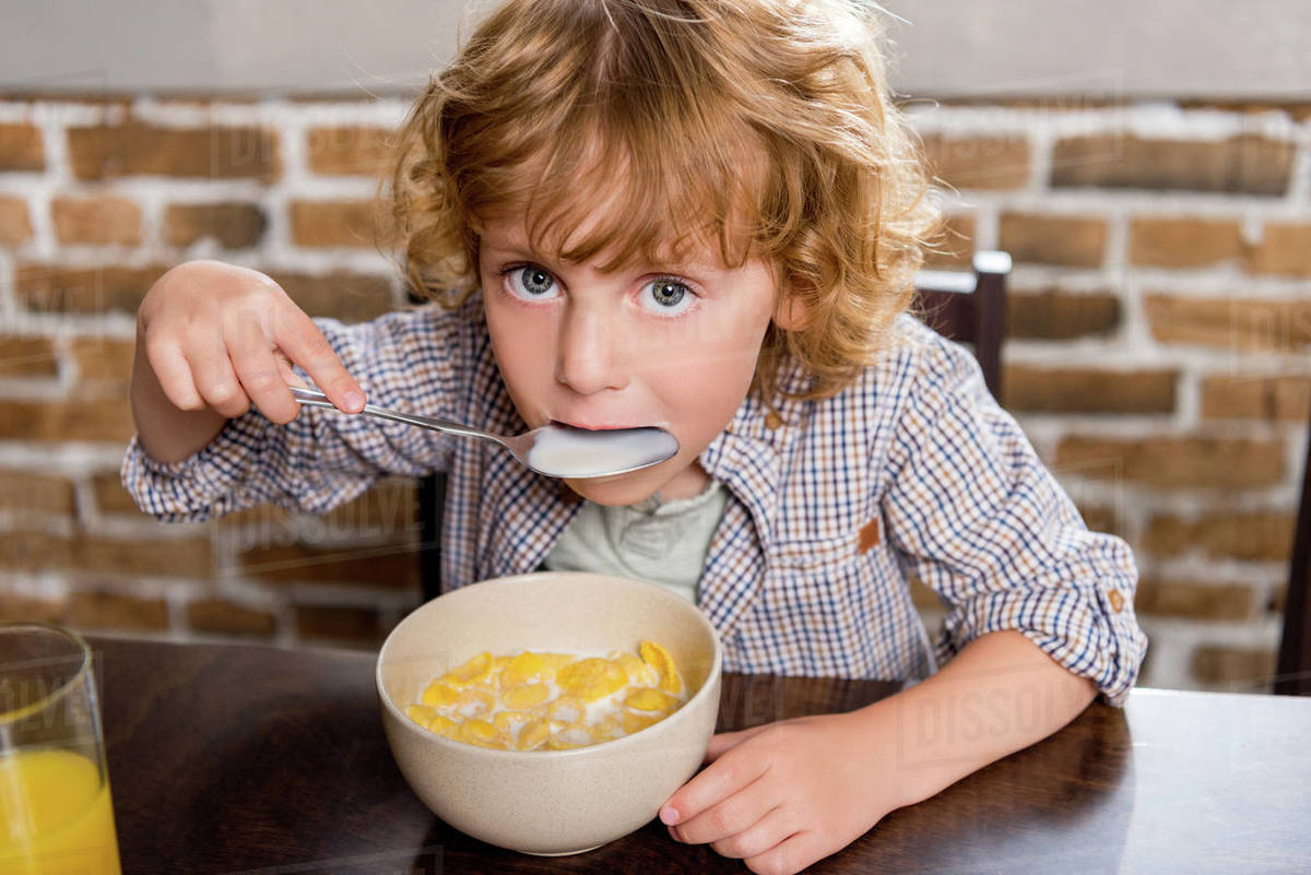 Adorable little boy eating corn flakes and looking at camera Stock