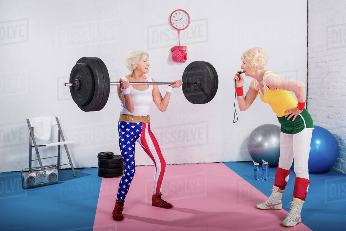 Senior female coach with whistle looking at senior sportswoman lifting