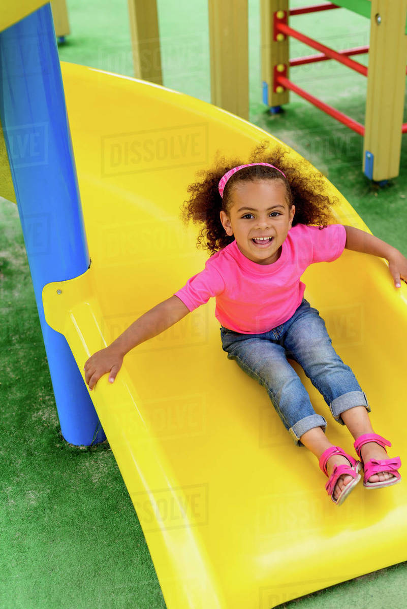 Smiling curly african american little kid sliding down from hill at