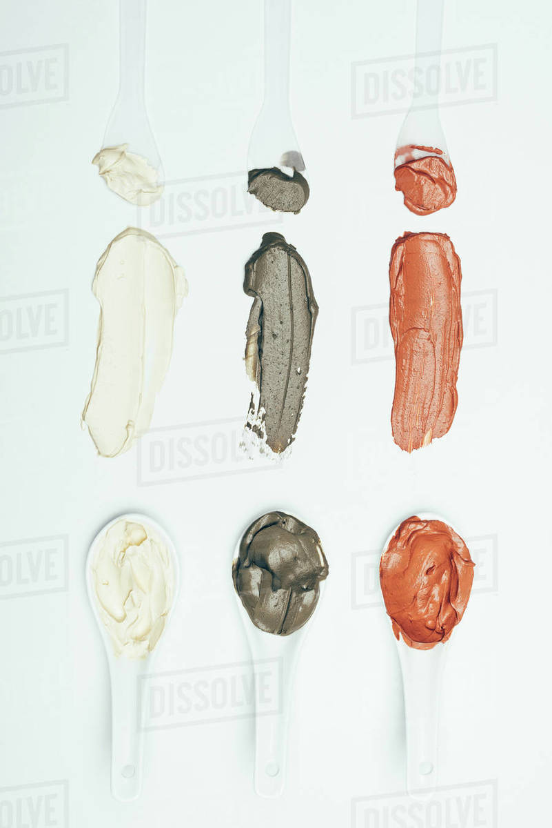 Flat lay with spoons and various colorful clay mask smudges placed in