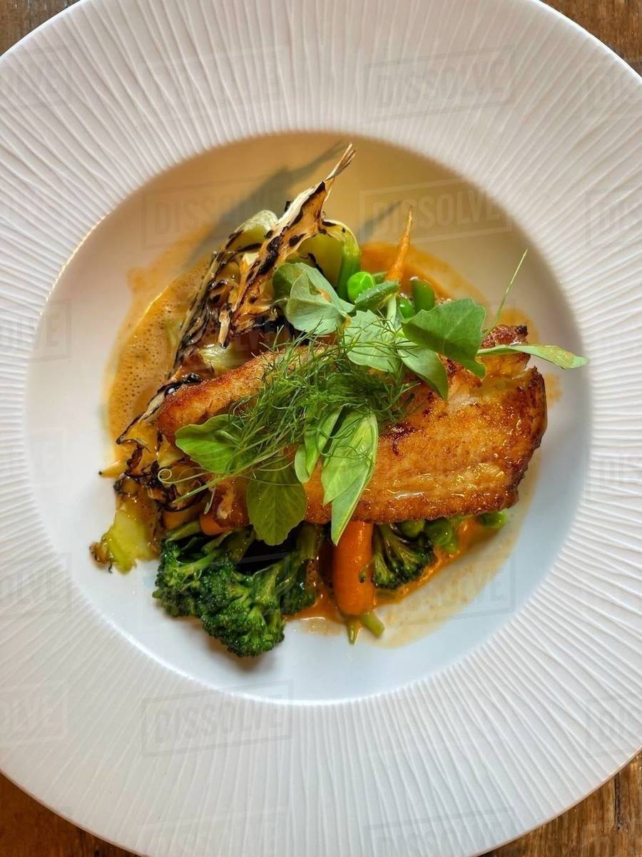 Overhead view of fried fish with broccoli, carrots, cabbage, pea shoots