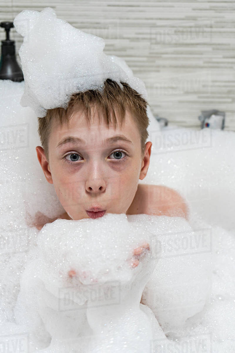 Boy sitting in a bubble bath blowing soap suds Stock Photo Dissolve