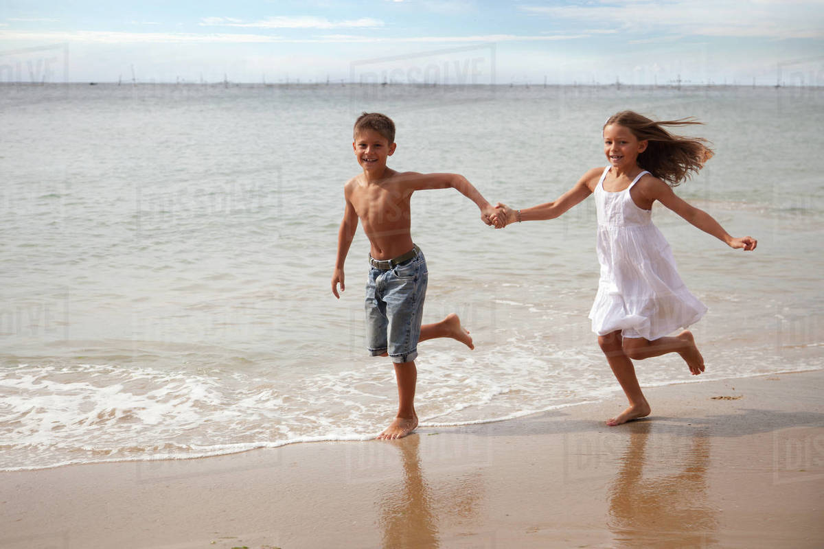 Boy and girl running along beach holding hands Stock Photo Dissolve