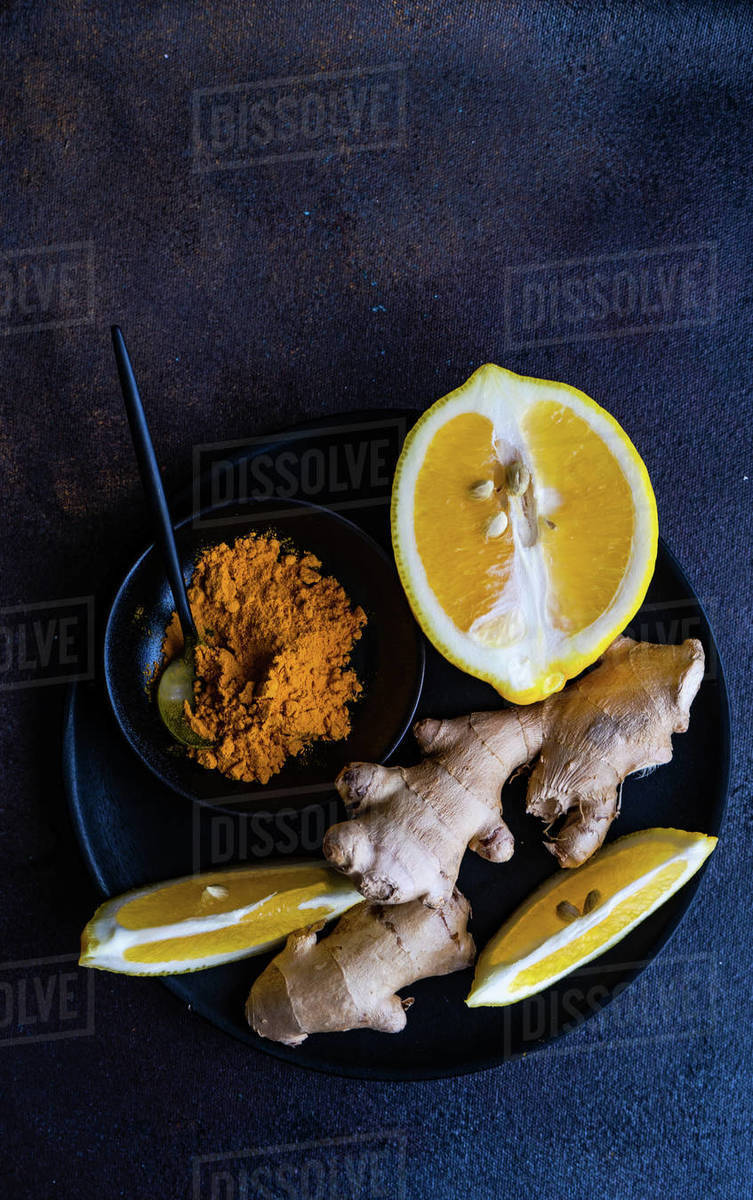 Overhead view of turmeric powder, ginger and fresh lemon on a plate