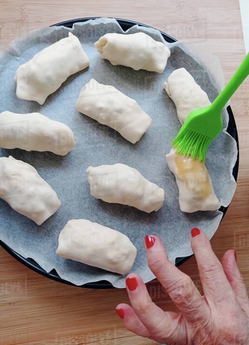 Overhead view of a woman brushing egg wash on homemade stuffed pastry