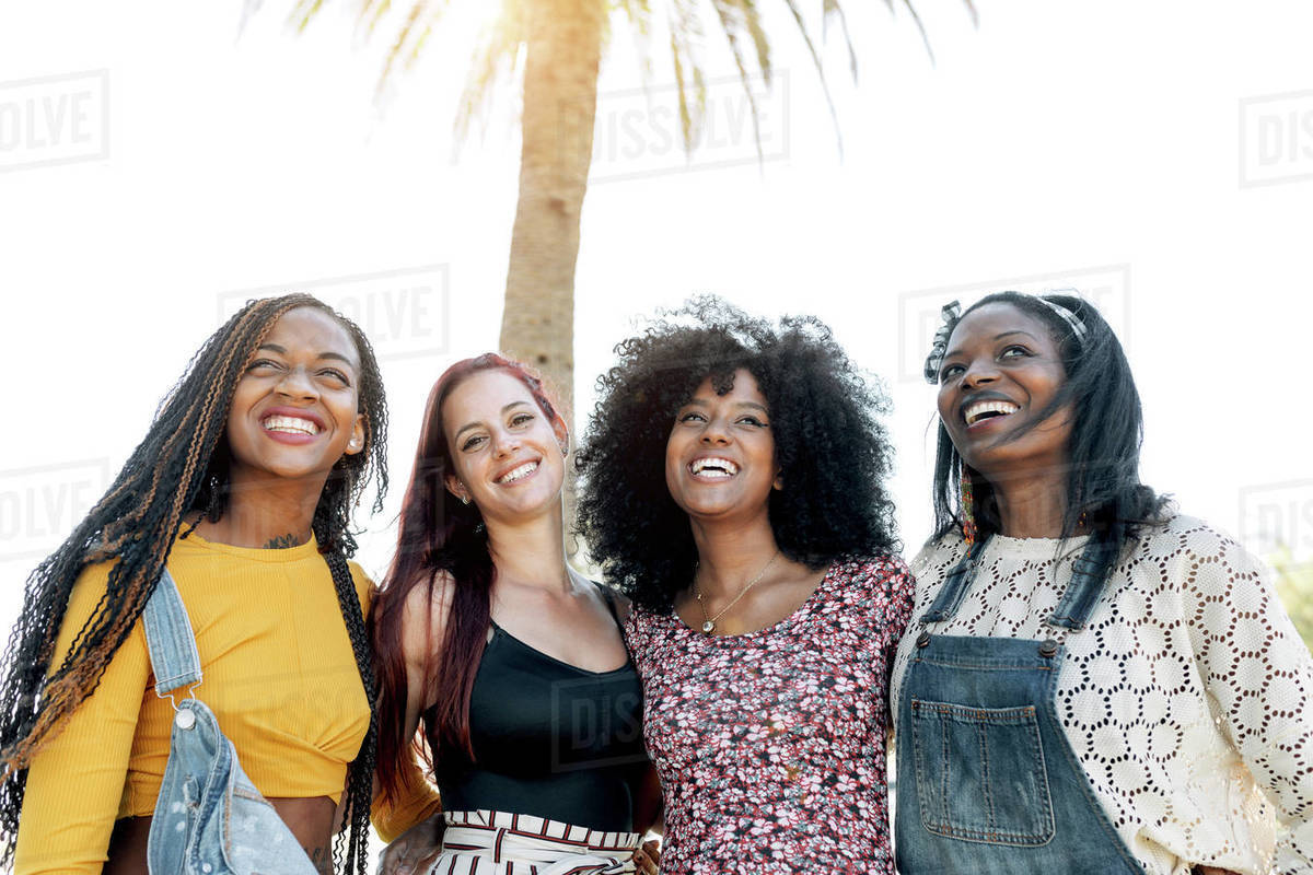 Friendly multiracial group of female friends cuddling on street while