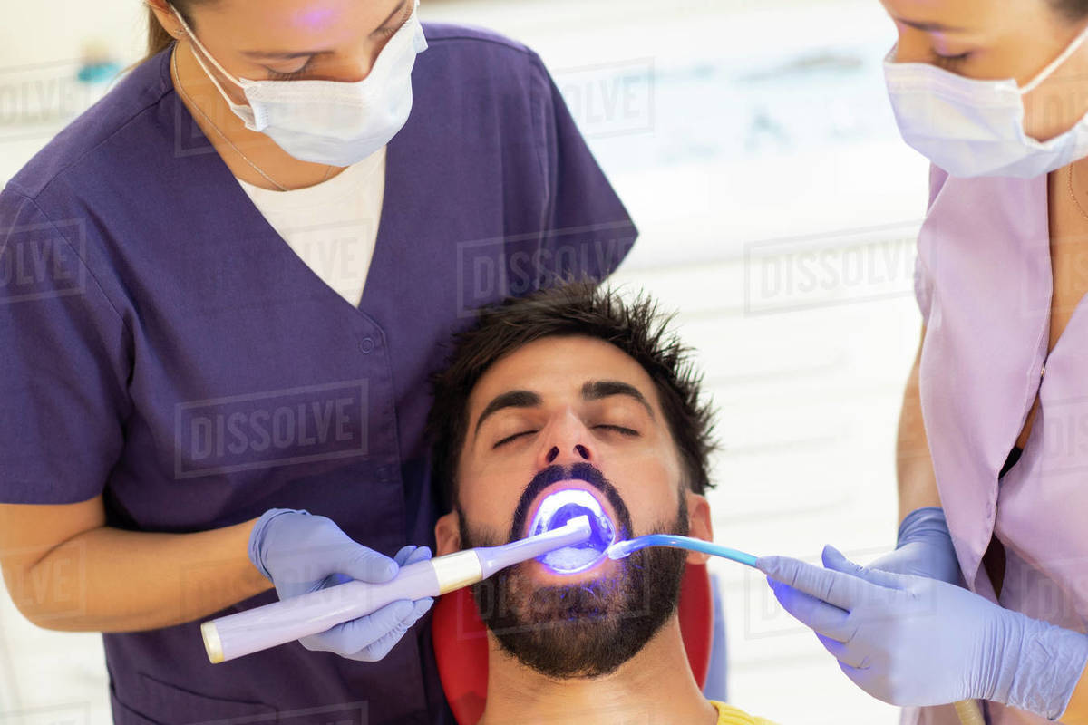 Female dentist and assistant using dental curing light and suction