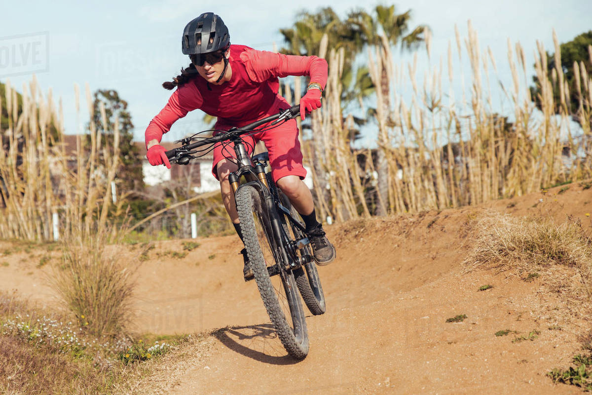 Sportswoman in black helmet and red sportswear with glasses riding mountain bike on training track Royalty-free stock photo