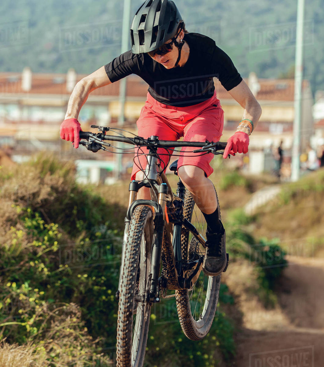 Sportswoman in black helmet and red sportswear with glasses riding mountain bike jumping in training track Royalty-free stock photo