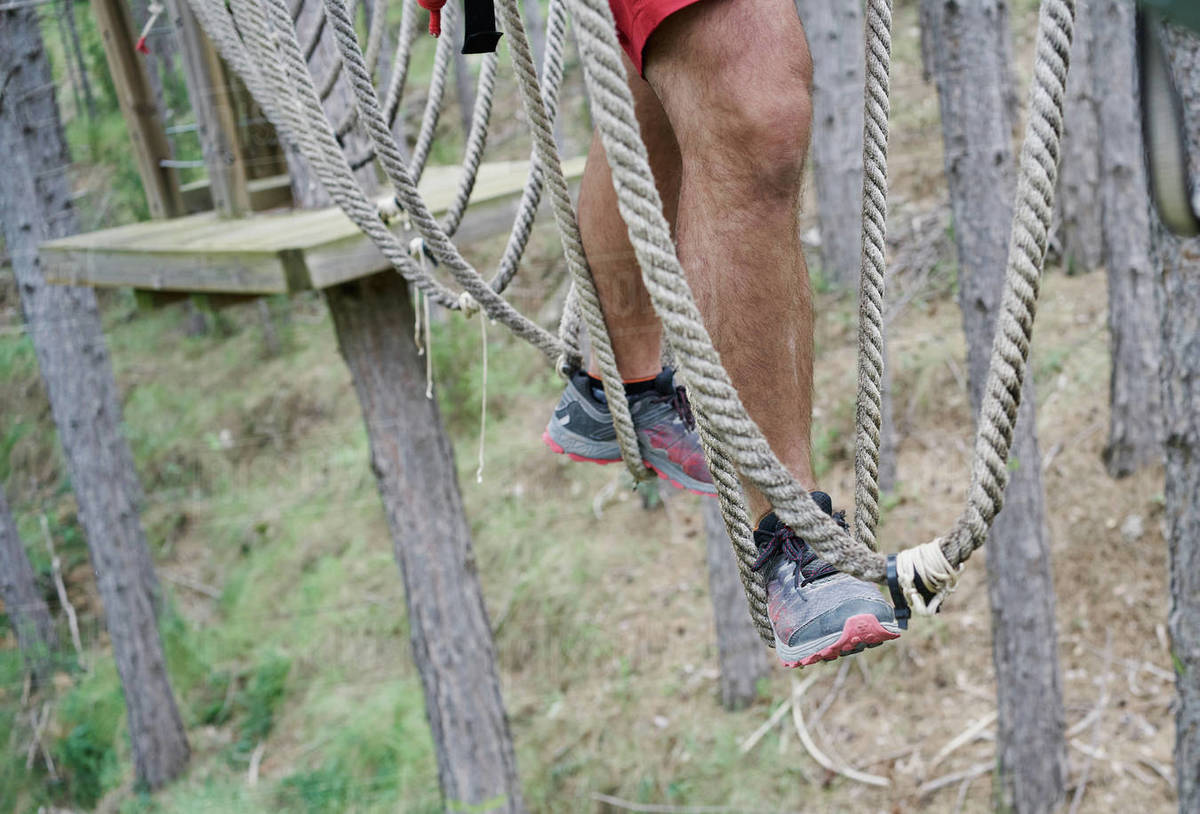 Unrecognizable male in sneakers walking on rope course in adventure park in forest Royalty-free stock photo