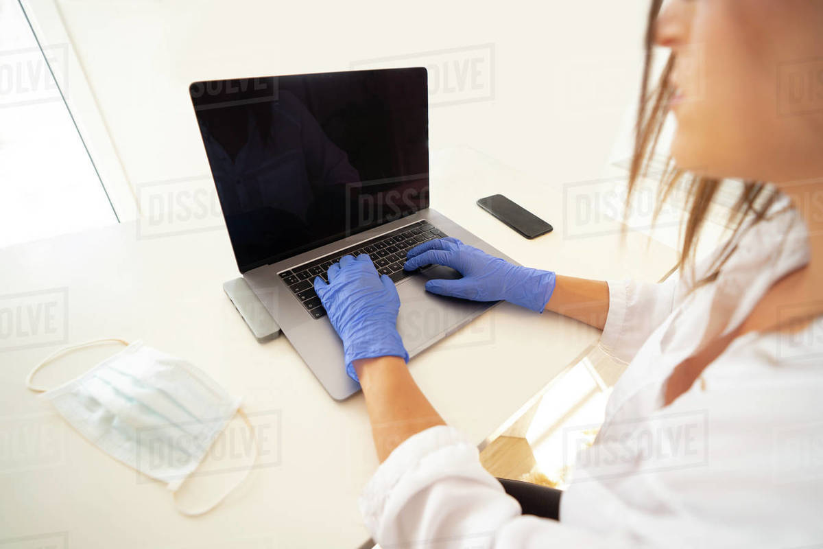 From above of crop anonymous female in latex gloves typing on laptop