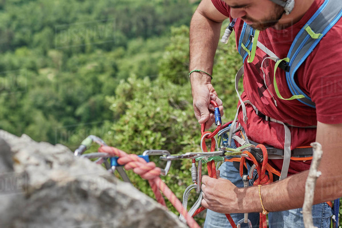 High angle of crop male alpinist in safety harness hanging on rope on