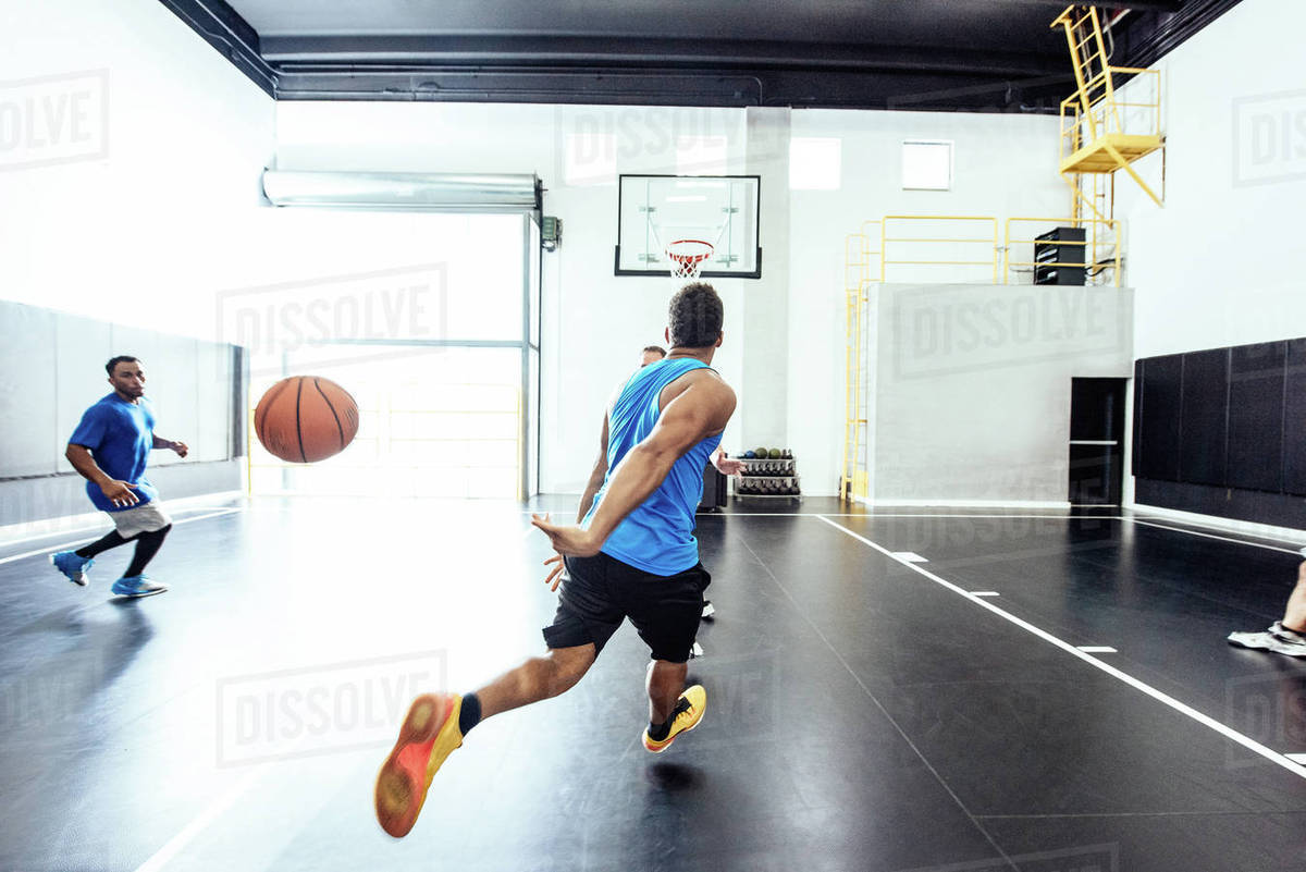 Two male basketball players running and passing ball on basketball court Stock Photo Dissolve