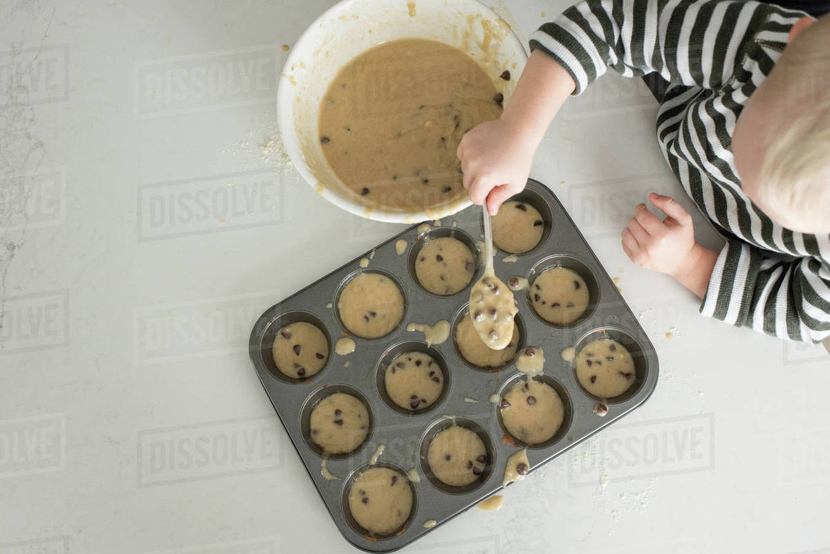 Young boy putting mixture into baking tray, overhead view Stock Photo