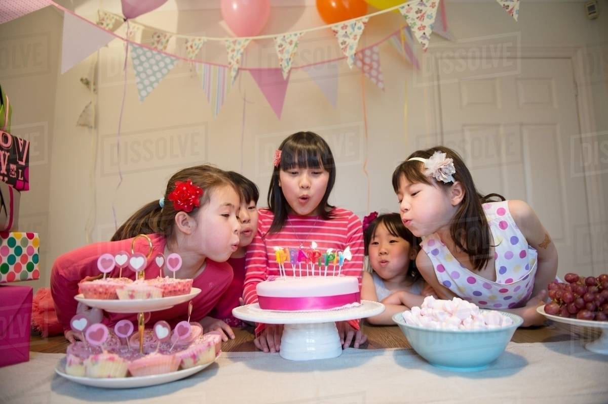Girls blowing out birthday candles on cake Stock Photo Dissolve