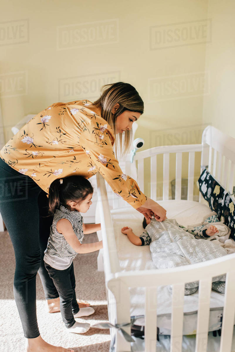 Girl and mother putting baby brother in crib Stock Photo Dissolve