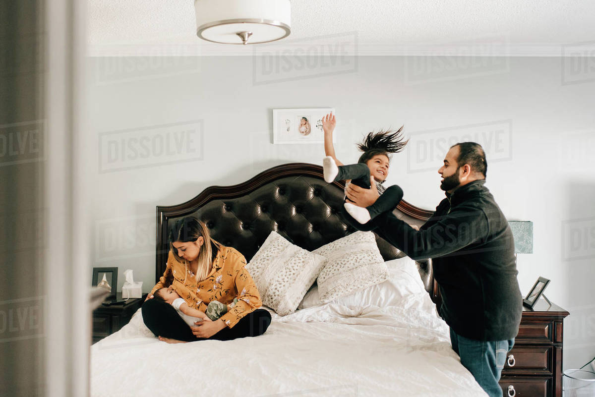 Girl being thrown onto bed by father, next to mother nursing baby brother Stock Photo Dissolve