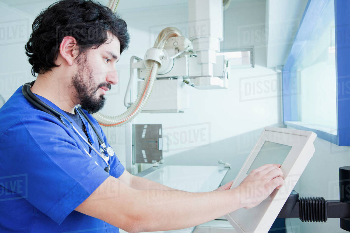 Young male radiographer operating X-ray machine control panel in ...