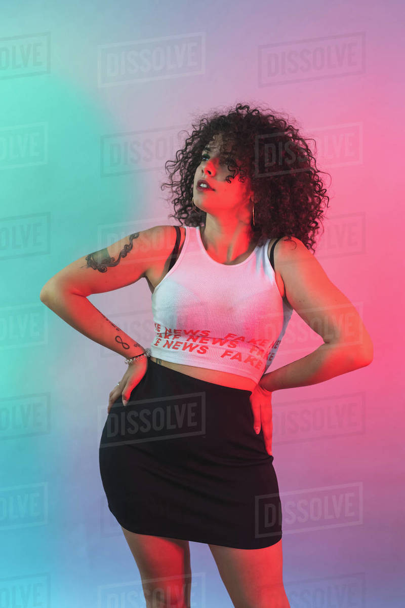 Young woman resting hands on hip against blue and pink background