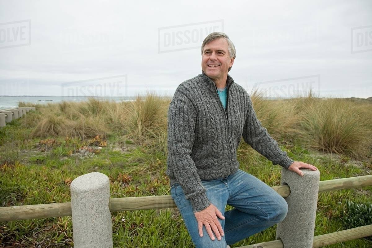 Man sitting on a fence at the coast Stock Photo Dissolve